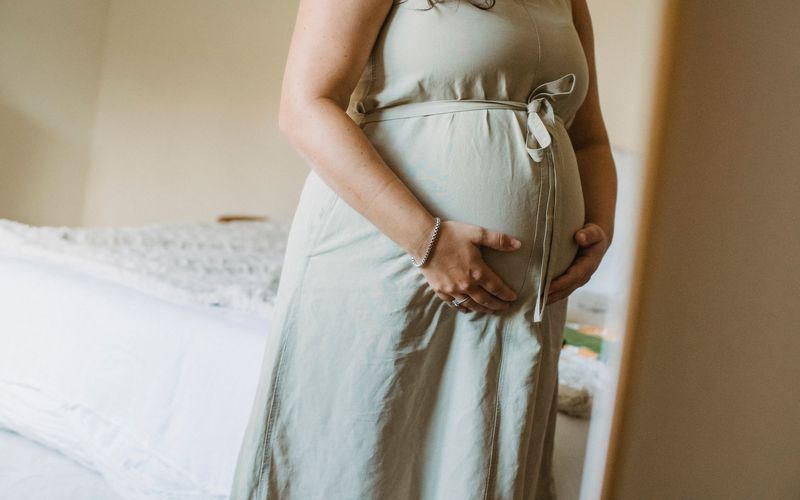 A pregnant woman holding her bump in soft daylight